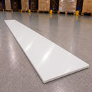 A long, rectangular white panel or board lies diagonally on a polished gray warehouse floor, with pallets and shelving visible in the blurred background.