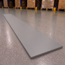 A long, rectangular gray mat or board placed diagonally on a warehouse floor, with pallets and shelving visible in the background.