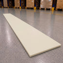 A long, rectangular off-white board or panel placed diagonally on a gray warehouse floor, with pallets and boxes visible in the blurred background.