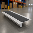 A single step ramp with a white textured frame and a black non-slip rubber tread, shown on a gray warehouse floor with shelves in the background.