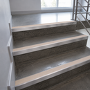 Concrete stair steps with light beige textured non-slip rubber treads installed along the edges, shown in an indoor stairwell with a metal railing.