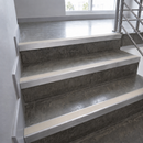 Concrete stair treads with white metal or rubber anti-slip strips installed on a set of indoor stairs with a metal railing.