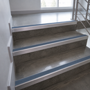 Concrete stair steps with blue anti-slip strips and silver metal handrails in an indoor stairwell.