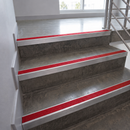 Red carpet stair grips installed on the risers of concrete stairs in a modern interior setting.