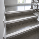 Gray concrete stair treads with white metal or painted risers and a stainless steel handrail in a bright modern stairwell.