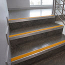 Concrete stairs with bright yellow textured anti-slip strips along the edges, shown in an indoor stairwell with a metal railing and window.