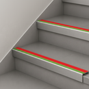 Red and green insert stair nosings fitted to two pale grey steps against a white stringer wall
