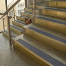 Brass stair nosings with regency blue-grey ribbed inserts on stone steps beside a glass balustrade