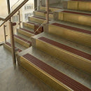 Brass stair nosings with rustic red ribbed inserts on stone steps beside a glass balustrade