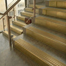Satin brass stair nosings with matching ribbed inserts on pale stone steps beside a glass balustrade