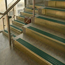 Brass stair nosings with spruce green castellated inserts on stone steps beside a glass balustrade