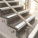 Raked back nosings with white ribbed inserts on mottled stone steps between stainless handrails