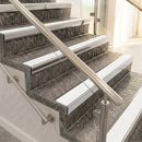Raked back nosings with white ribbed inserts on mottled stone steps between stainless handrails