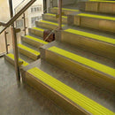 Brass stair nosings with bright yellow ribbed inserts on stone steps beside a glass balustrade