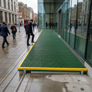 Green anti-slip GRP grating walkway with yellow safety trim installed outside modern glass building
