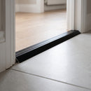 Black anodised aluminium ramp threshold fitted across an internal doorway, bridging pale oak laminate down to grey porcelain floor tile