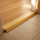 Gold anodised aluminium ramp threshold fitted at a landing doorway between engineered oak boards and lower beige ceramic tile