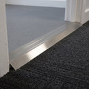 Inox brushed-finish aluminium ramp threshold fitted in an office doorway between grey sheet vinyl and lower dark carpet tile