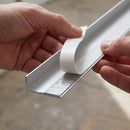 Protective paper backing being peeled from the factory-applied self-adhesive tape on the underside of a silver aluminium ramp threshold