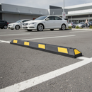 Black and yellow rubber car park wheel stop bolted down at the head of a parking space in an outdoor retail car park with cars parked behind it