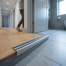 Aluminum stair nosing with anti-slip strips installed on wood step edge leading to tiled bathroom