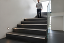 Anti-slip bullnose stair nosing with Black insert — installed on UK staircase, semi-rounded profile with person using stairs
