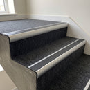 Aluminium bullnose stair nosing with a black anti-slip insert fitted to carpet-tiled concrete steps in an office stair core