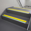 Aluminium bullnose stair nosing with a yellow anti-slip insert and green photoluminescent strip fitted to grey vinyl steps in a public stairwell