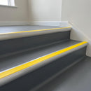 Aluminium bullnose stair nosing with a high-visibility yellow anti-slip insert fitted to dark vinyl steps on an internal works stair