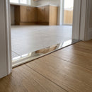 38mm aluminium cover strip in Bright polished finish fitted in a hallway doorway between oak-effect LVT and porcelain tile