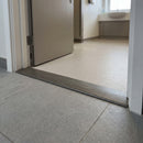 38mm aluminium cover strip in Brushed Stainless fitted in a washroom doorway between safety vinyl and grey tile