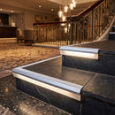 White insert aluminium LED stair nosing on dark slate hotel steps, riser diffuser glowing warm white