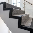 Black coated pre-formed stair side angles finishing the open-string edge of grey carpeted steps in a stairwell