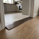 Bronze aluminium ramp threshold strip 38mm screw fitted where tile meets a lower oak-effect LVT floor in a kitchen doorway