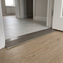 Brushed stainless aluminium ramp threshold strip 38mm screw fitted between a raised tile floor and oak LVT in a hallway