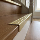 Matt brass aluminium stair nosing 25mm x 10mm fitted over the front edge of a warm laminate stair tread above a white painted riser