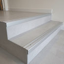 Aluminium stair nosing screw-fixed to two grey tiled steps in a commercial entrance, deep front face covering the step edge