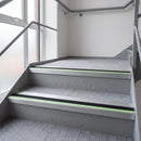 57x55mm rake back aluminium stair nosing with black PVC insert and green photoluminescent nose strip fitted along carpeted office stairs