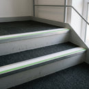 57x55mm rake back aluminium stair nosing with white PVC insert and green photoluminescent nose strip fitted in a commercial stairwell
