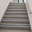 Aluminium rakeback stair nosings with midnight grey anti-slip inserts fitted to every step of a grey tiled internal staircase