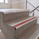 Red insert 70x40mm bullnose aluminium stair nosing with photoluminescent strip fitted along two concrete steps in a commercial stairwell