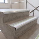 White insert 70x40mm bullnose aluminium stair nosing with photoluminescent strip fitted along two concrete steps in a commercial stairwell