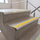 Yellow insert 70x40mm bullnose aluminium stair nosing with photoluminescent strip fitted along two concrete steps in a commercial stairwell