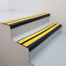 Satin black aluminium bullnose stair nosing with twin yellow inserts fitted to a public building stairwell step