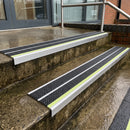 Black Tredsafe 91x32mm aluminium stair nosings fitted to wet exterior entrance steps, green photoluminescent strip along each step edge