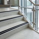 Twin-insert rakeback aluminium stair nosing with black anti-slip inserts fitted along concrete steps in a glazed office stairwell