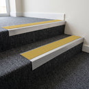 Mill finish aluminium stair nosing with Yellow insert fitted to dark grey carpet on a factory office stair