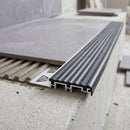 Trapezoid-perforated anchoring leg of the 52mm aluminium stair nosing bedded into combed tile adhesive with the stair tile laid over it