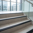 Wide 52mm aluminium tile-in stair nosing with GS Black RAL 9011 ribbed insert forming the step edge on a pale tiled office stair