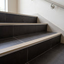 Wide 52mm aluminium tile-in stair nosing with HB Light Beige RAL 1019 ribbed insert on dark charcoal tiled stairs